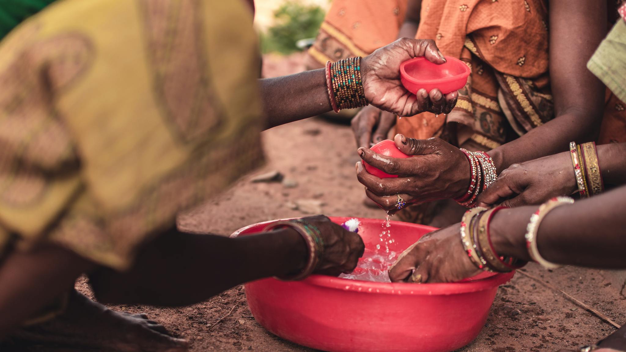 South Asian women washing hands with bowls, showcasing traditional wear and cultural practices in Odisha, India.